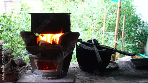 In a simple and old-fashioned way, cooking food with a stainless steel pot and an Anglo charcoal stove. to get a dark sooty color over a long time. The charcoal stove has a red light on it.