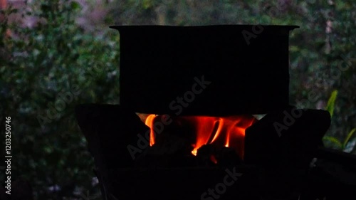 In a simple and old-fashioned way, cooking food with a stainless steel pot and an Anglo charcoal stove. to get a dark sooty color over a long time. The charcoal stove has a red light on it.