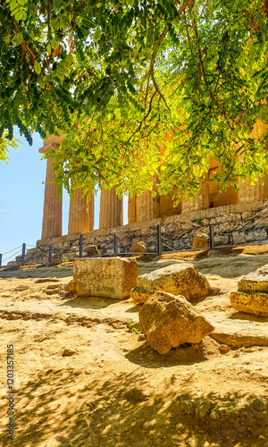 Una vista mozzafiato del Tempio della Concordia nella Valle dei Templi ad Agrigento, Sicilia, incorniciato da un rigoglioso albero verde. La luce del sole filtra tra le foglie photo