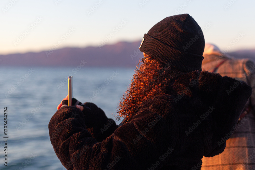 Young girl in a black beanie and heavy jacket observes Lake Garda at sunset