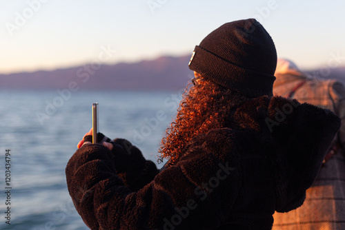 Obraz na płótnie Young girl in a black beanie and heavy jacket observes Lake Garda at sunset w salonie