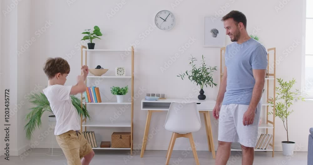 Confident little boy in casual clothes practicing karate in living room, showing his father martial arts moves. Smiling father nodding approvingly, watching his son performing kung fu fighting stances