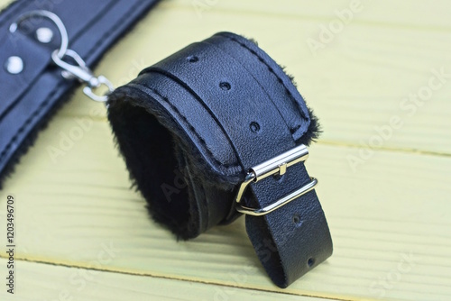 black gaming leather role play handcuffs with fur and metal gray chain lies on yellow wooden table in room