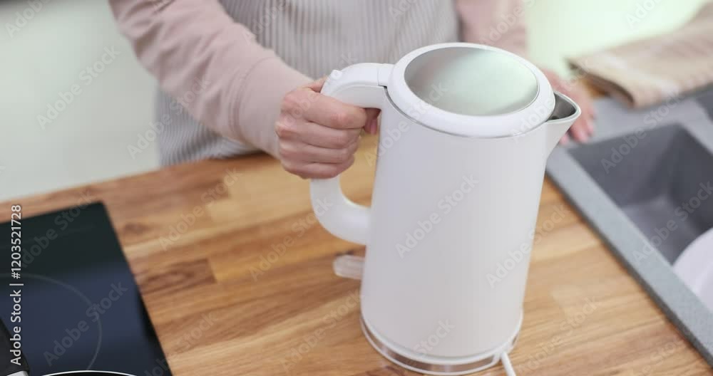 Woman hand puts electric kettle turning on kitchen device. Housewife in apron waits for boiled water to brew aromatic tea for lunch slow motion Woman hand puts electric kettle turning on kitchen device. Housewife in apron waits for boiled water to brew aromatic tea for lunch slow motion