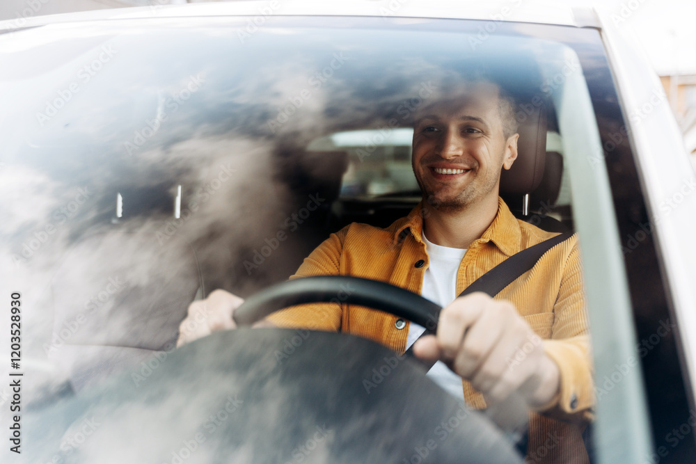 Naklejka premium Handsome young man is smiling while sitting in his new car