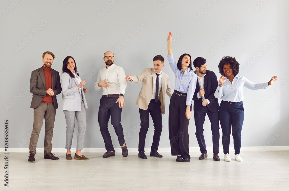 Obraz premium Group portrait of joyful smiling multiracial business team standing in row against grey wall and having fun at end of work day. Happy cheerful company employees dancing together, celebrating weekend.