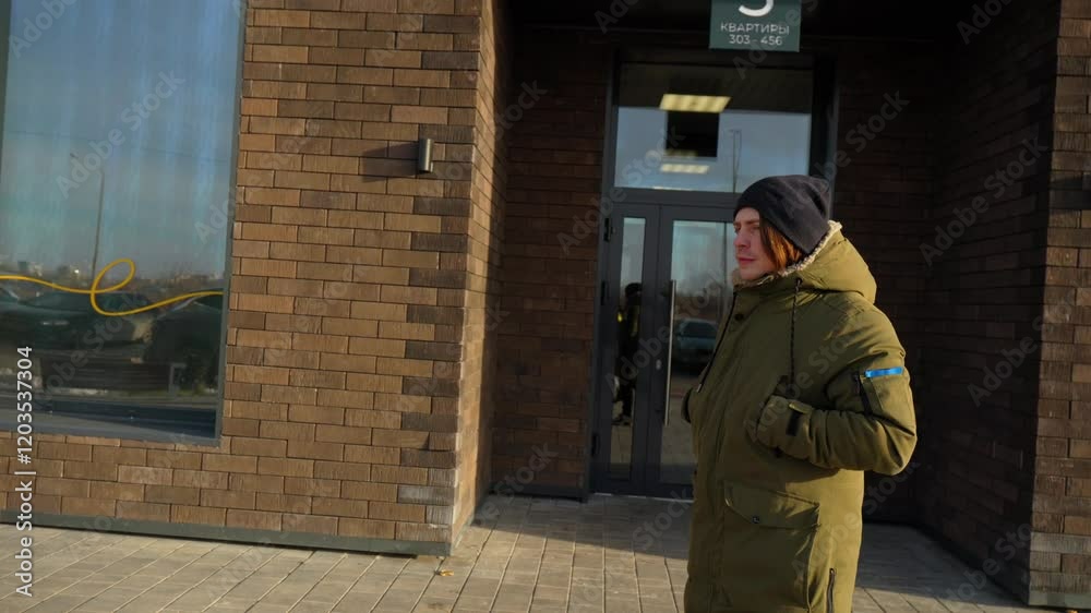 Bright sunlight shines on a person dressed warmly in a cozy coat and hat, strolling down a modern city street lined with buildings and parked cars, embodying winter charm. Bright sunlight shines on a person dressed warmly in a cozy coat and hat, strolling down a modern city street lined with buildings and parked cars, embodying winter charm.