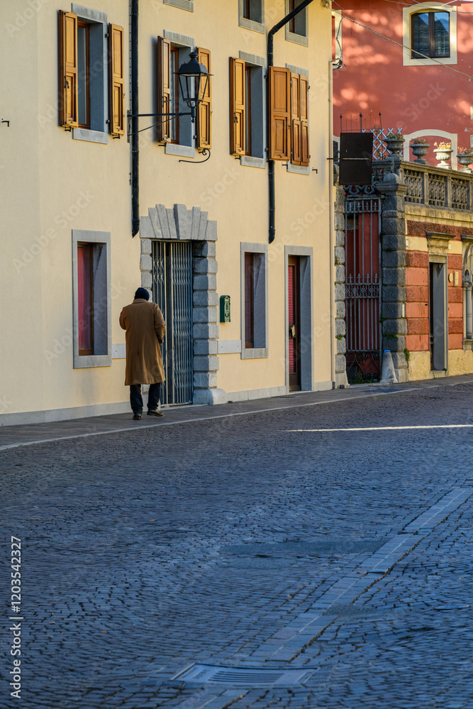 Obraz premium Cobblestone street, old buildings, and a passerby.