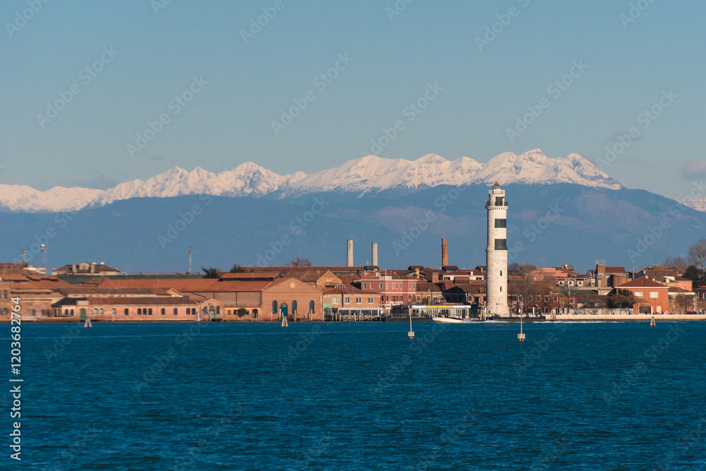 Fototapeta premium Panorama dell’isola di Murano e del suo faro con le Dolomiti coperte di neve sullo sfondo, in una giornata invernale