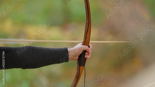 A man is holding a bow and arrow, ready to shoot. Concept of focus and determination, as the man prepares to take aim. The bow and arrow are the main objects in the scene