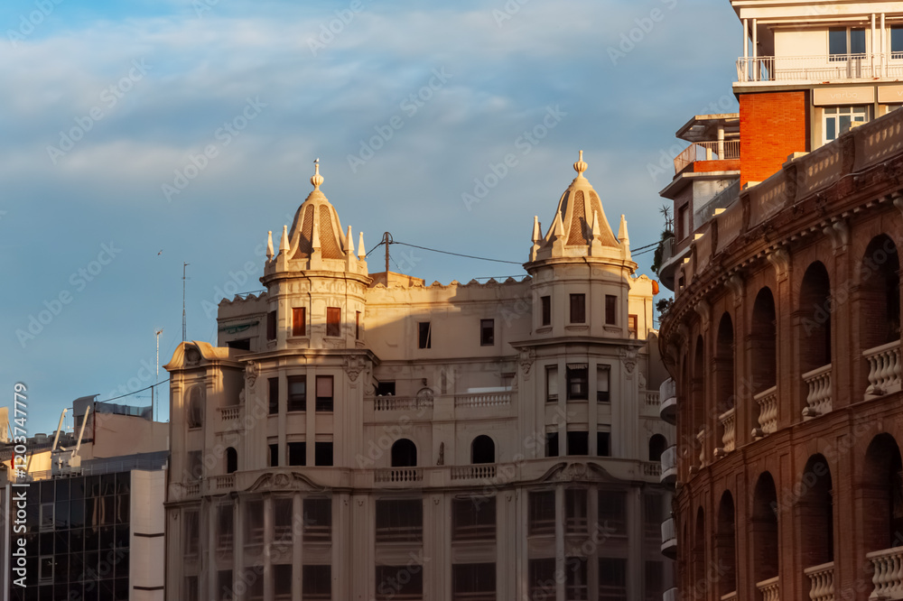 Obraz premium Sunlight casting golden glow on modernist architecture with domed towers near valencia bullring, highlighting contrasting architectural styles during sunset hour