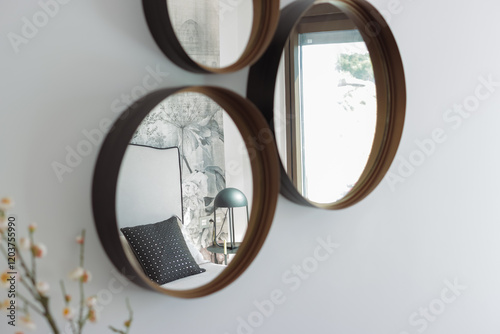 Three round mirrors with wooden frames are hanging on a white wall, reflecting a modern bedroom interior with floral wallpaper, a comfortable bed, and a stylish lamp