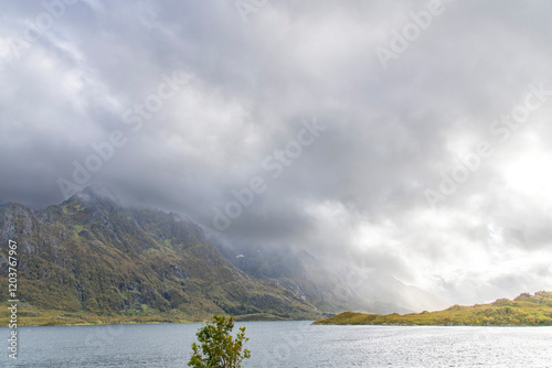 Dramatic landscape with cloud cover over mountain range on island of Austvagoya along a fjord on the Lofoten island chain archipelago in Norway with sun glistening on wet environment photo