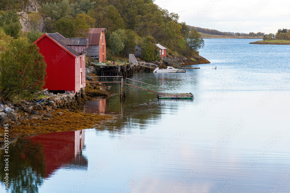 Obraz premium Tranquil water of a fjord on the Lofoten island chain in Norway with traditional red fisherman cabins (rorbu) along the shore reflected in water
