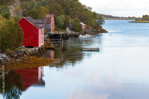 Tranquil water of a fjord on the Lofoten island chain in Norway with traditional red fisherman cabins (rorbu) along the shore reflected in water photo