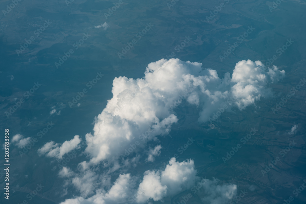 View from above of fluffy cloud formation with a landscape visible below. Clouds are white and dense, contrasting with the darker terrain beneath, Visual of the earth's atmosphere and surface.
