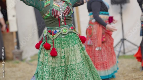 A woman in a green dress with red pom poms is dancing with other women. Scene is lively and festive