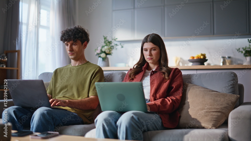 Home sweethearts browsing laptops at soft couch place. Young couple working