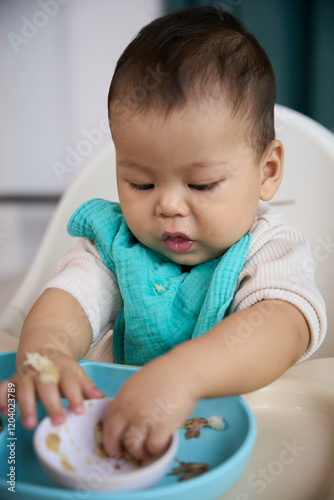 The baby is picking up food in the cup