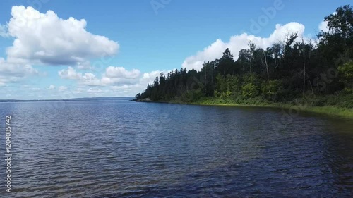 Natural landscape with calm waters on the shore of a freshwater lake, lush green trees and clouds in the blue sky. Lac Matapedia, Quebec, Canada. photo