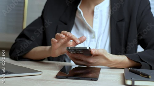 Business woman using a smartphone in a modern office, close-up. Woman in suit using mobile phone and laptop at office desk
