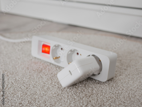 Extension cord with red switch and charger on carpet consuming energy