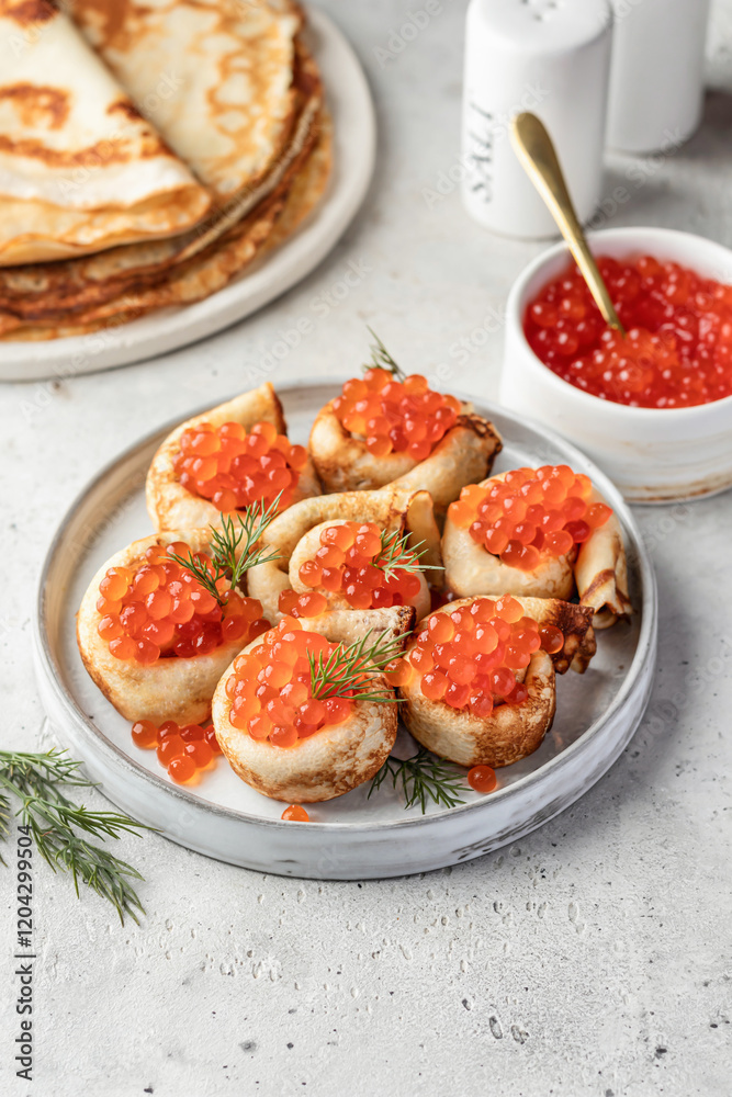 Pancake day, maslenitsa. Crepes, pancakes rolled with red caviar on white plate, gray background with text space Pancake day, maslenitsa. Crepes, pancakes rolled with red caviar on white plate, gray background with text space