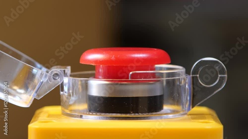 Red industrial button with open protective cover, side view of an emergency factory switch, shaky camera close-up, safety control panel, machinery power button, industrial equipment detail simple shot photo