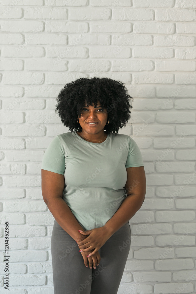 Laughing millennial African American woman with an afro hairstyle and good sense of humor smiling and laugh on brick wall at home background. Copy space. Happiness and good emotions concept