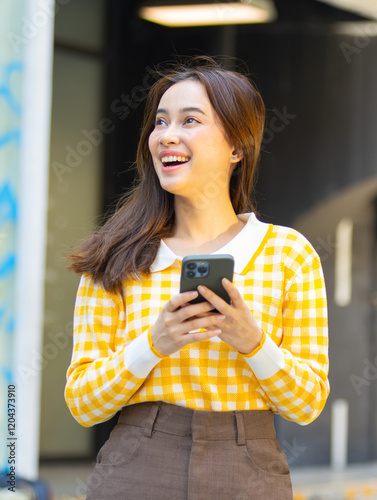 Smiling Attractive young woman using mobile phone while walking walking the streets of the city. Happy Woman using smartphone browsing internet, typing message, social media enjoy weekend outdoors.