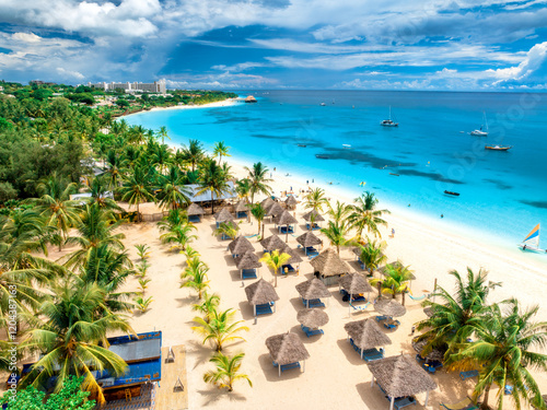 Fototapeta Naklejka Na Ścianę i Meble -  Aerial view of white sandy beach with palm trees, umbrellas, yachts, boats, blue ocean, sky with clouds at sunset. Summer holiday in Kendwa, Zanzibar island. Tropical landscape. Clear sea. Top view
