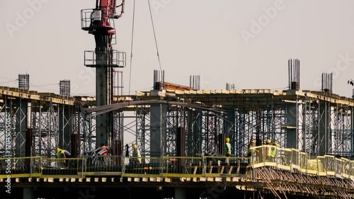 Unidentified construction workers carry rebars carried by a crane on top of the building. Time-lapse of unrecognizable construction workers.