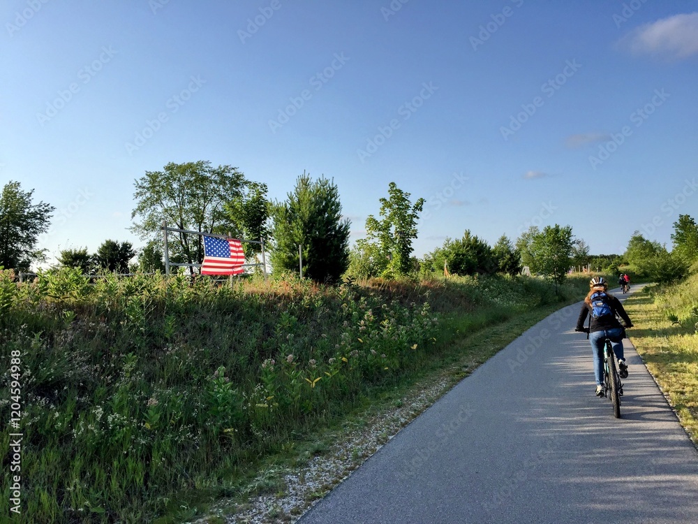 Obraz premium Woman Riding Bike On Trail Near American Flag