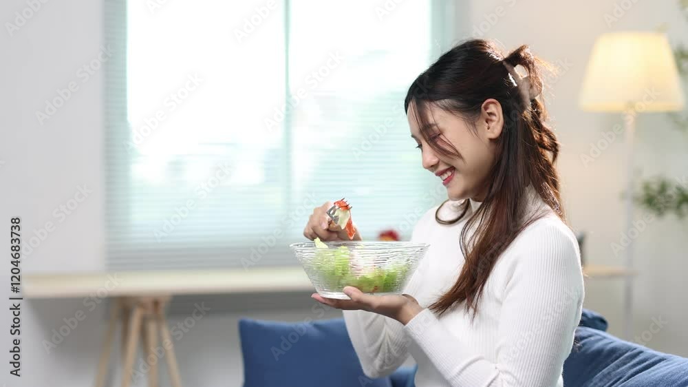 Young woman sits comfortably on a sofa, savoring a fresh and delicious salad. Enjoying her meal, she radiates happiness and contentment in a relaxed home. Young woman sits comfortably on a sofa, savoring a fresh and delicious salad. Enjoying her meal, she radiates happiness and contentment in a relaxed home.