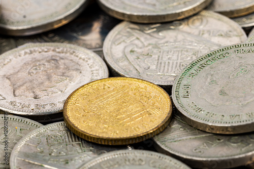 Close-up of Spanish pesetas from the Franco era, highlighting a golden coin in focus.