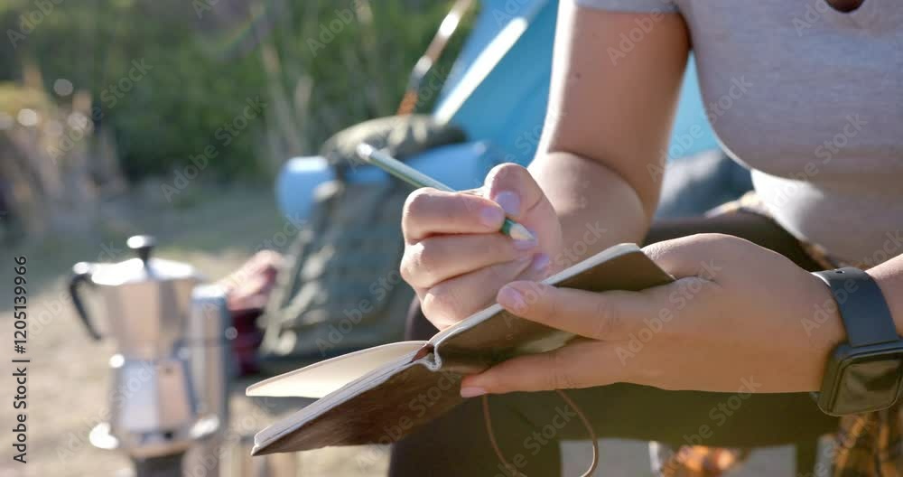 Writing in journal, woman sitting outdoors during mountain hike with camping gear