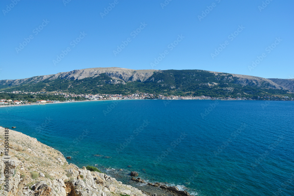 Rocky landscape of the western part of Baska Bay, where steep cliffs descend towards the blue sea with Baska village and beach visible in the distance Rocky landscape of the western part of Baska Bay, where steep cliffs descend towards the blue sea with Baska village and beach visible in the distance