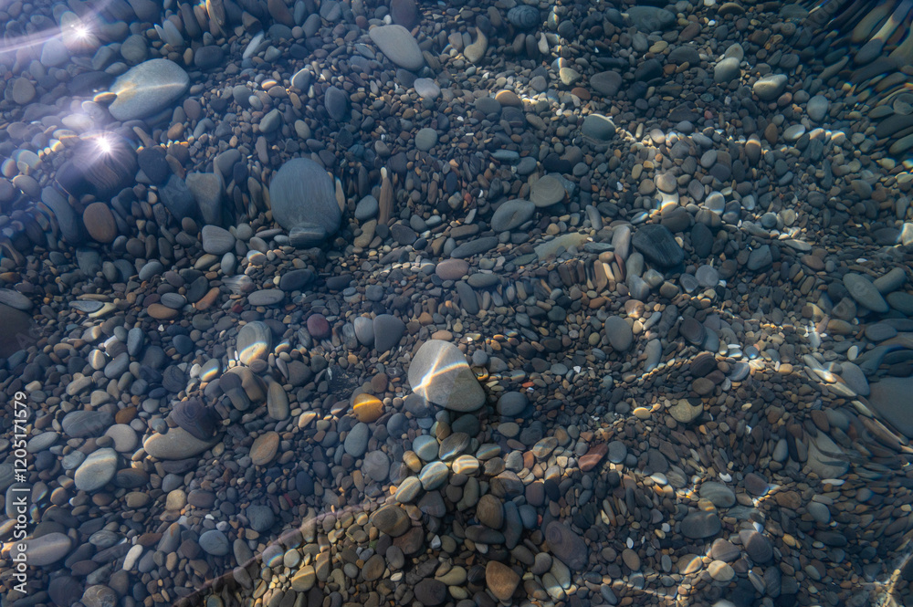 Underwater pebble backgrounds. Colorful stones sea bottom in the sun rays. View from above through clear water. Seascape wallpaper texture. Defocus.