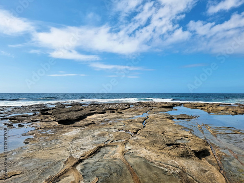Waves rolling over the rocks near the Cowrie Hole, Newcastle, New South Wales, Australia. Blue sky with white clouds  photo