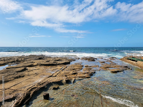 Waves rolling over the rocks near the Cowrie Hole, Newcastle, New South Wales, Australia. Blue sky with white clouds  photo