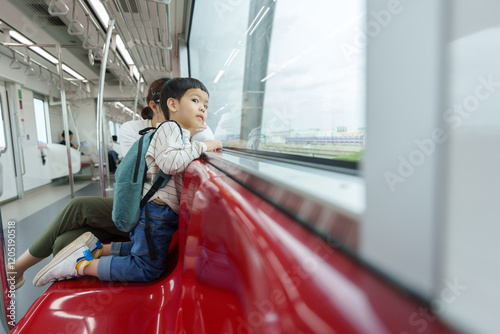 Wallpaper Mural Asian child with a backpack traveling on an elevated public train with his mother, looking out the window during their journey to school or an outing. Torontodigital.ca