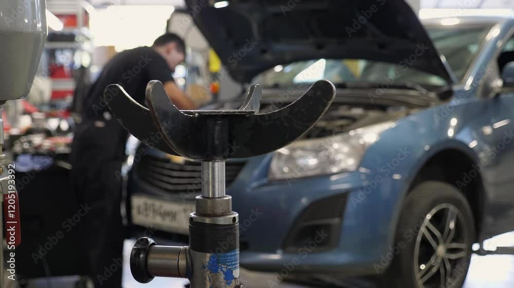 The car is undergoing maintenance at a service station, a mechanic is repairing the engine under the hood, and working tools are in the foreground.