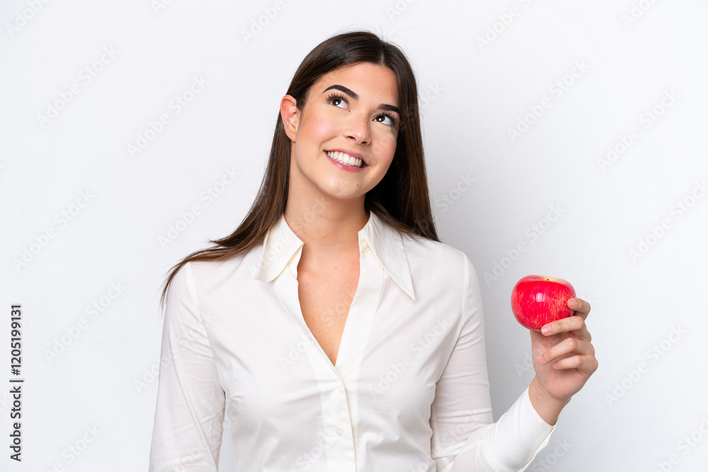 Young Brazilian woman with an apple isolated on white background looking up while smiling Young Brazilian woman with an apple isolated on white background looking up while smiling