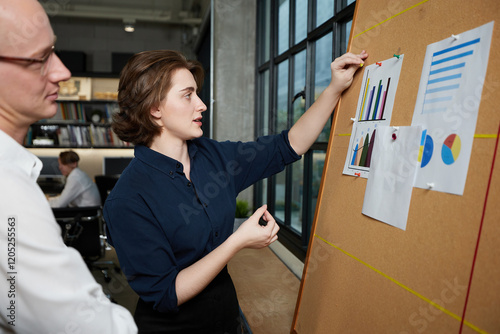businesswoman and businessman looking at business chart paper on bulletin board in the office