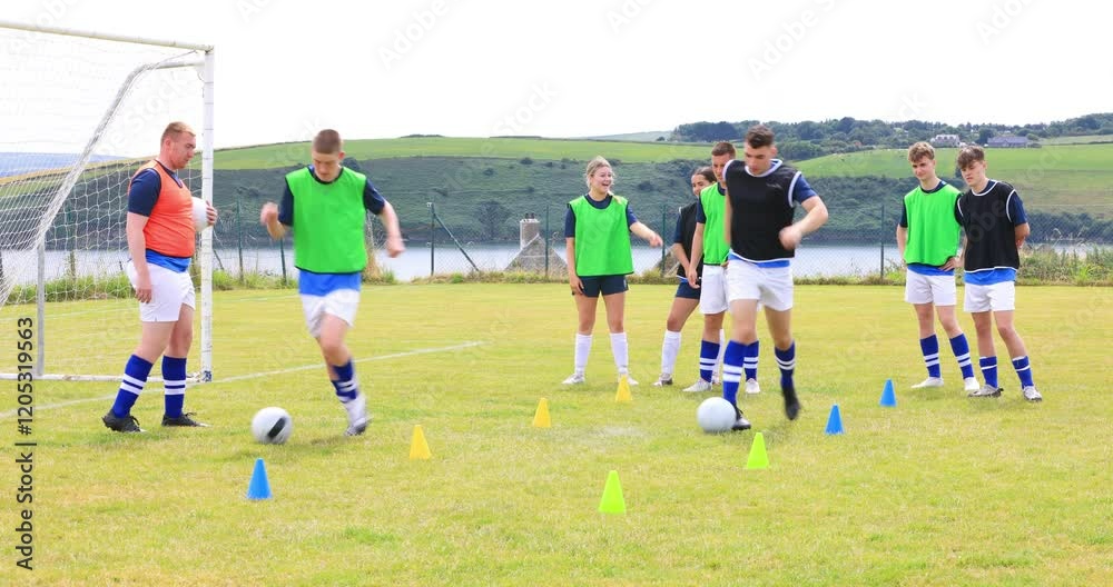 Male and female soccer players running after ball and avoiding cones with coach on pitch Male and female soccer players running after ball and avoiding cones with coach on pitch