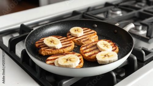 Within the sleek setting of a modern white kitchen, banana slices and brioche bread sizzle on a non-stick pan over a gas stove, setting the stage for an enticing grilled peanut butter banana sandwich.