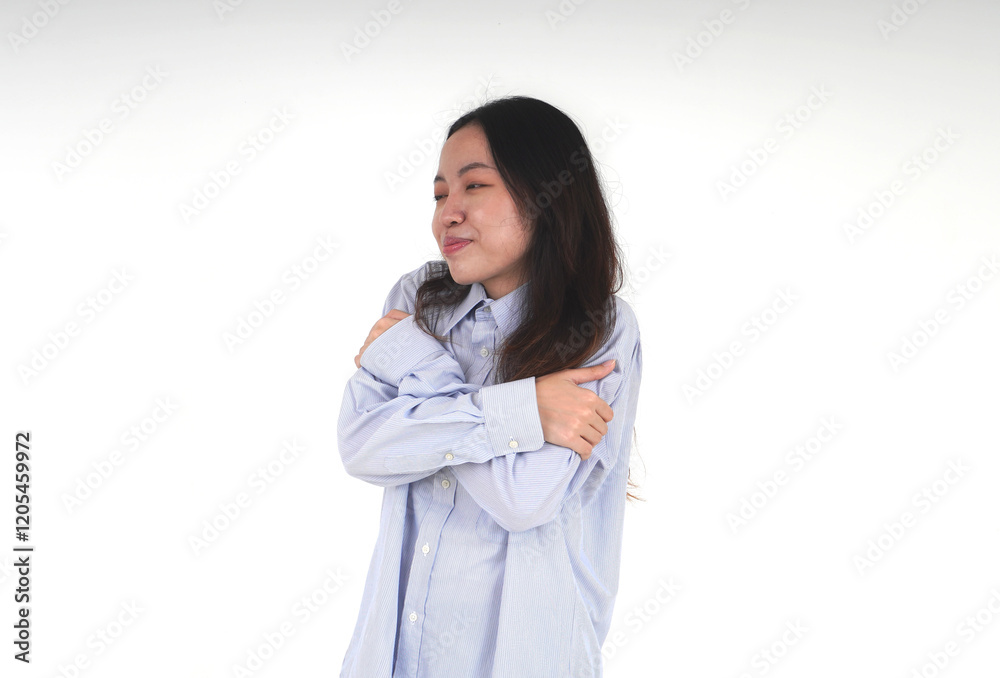 Asian women with light blue shirt and long hair hugging herself. Self love themed photo isolated on horizontal white background from slightly side angle view. Asian women with light blue shirt and long hair hugging herself. Self love themed photo isolated on horizontal white background from slightly side angle view.