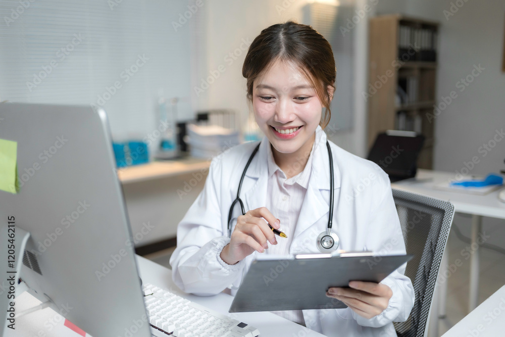 Young female physician smiling and working with computer and taking notes on clipboard in her bright modern office Young female physician smiling and working with computer and taking notes on clipboard in her bright modern office