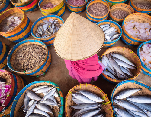 A asiatic woman wearing a straw hat stands in front of a basket of fish photo