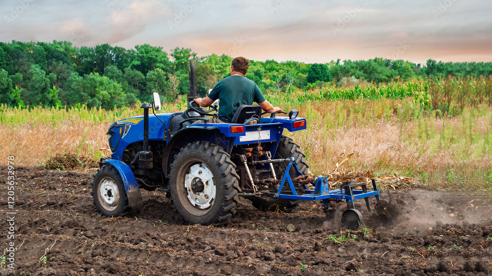 A farmer plowing a field on a small blue tractor, preparing the soil for planting crops.